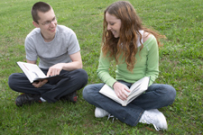 two students sitting on a lawn, with books open and in discussion